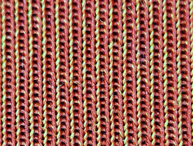 Back side of the innovative knitted fabric. The red yarn is plated only on one side of the stitch so that the yellow yarn is still visible on the other half.